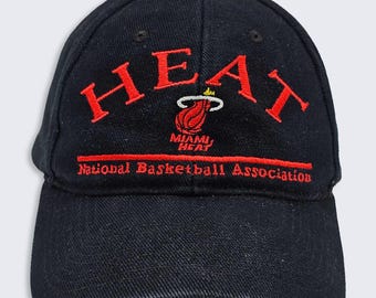 May include: Black baseball cap with the word "HEAT" embroidered in red across the front. Below the word "HEAT" is the Miami Heat logo and the text "National Basketball Association" in red.