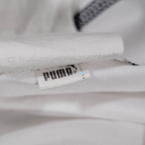 K&ouml;nnte beinhalten: Nahaufnahme eines wei&szlig;en Puma-Logos mit dem Text "CZ Pouze proci prostředek pro jemn&eacute; pr&aacute;dlo" auf Tschechisch.