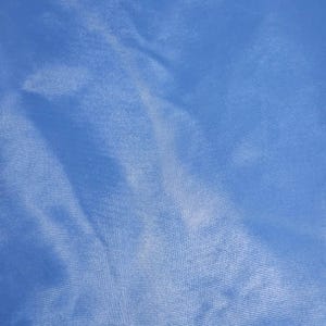 May include: A close-up shot of a light blue fabric with subtle folds and a textured surface. The fabric appears to be smooth and shiny, reflecting light in a soft, diffused manner. The overall effect is one of gentle movement and fluidity.
