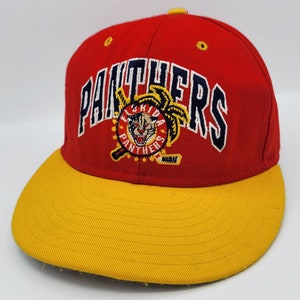 Op de afbeelding: Een rode en gele baseballcap met het Florida Panthers-logo. De cap heeft een rode kroon en een gele klep. Het logo bevat het woord "PANTHERS" in marineblauw en een cirkelvormig embleem met een panterkop.