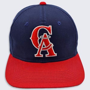 Op de afbeelding: Een marineblauwe en rode baseballpet met het logo van de Los Angeles Angels of Anaheim. Het logo is een rode "A" met een halo erboven, omringd door een witte omtrek. De pet heeft een rode klep.