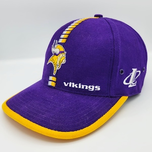 Könnte beinhalten: Lila und gelbe Baseballkappe mit dem Logo der Minnesota Vikings und dem Wort "vikings" auf der Vorderseite gestickt. Die Kappe hat einen gelben Schirm und einen weißen und gelben Streifen an der Seite.