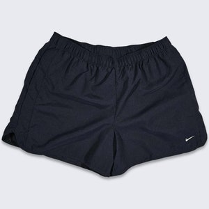 Może przedstawiać: Czarne spodenki sportowe z białym logo Nike w kształcie zygzaka na prawej nogawce.