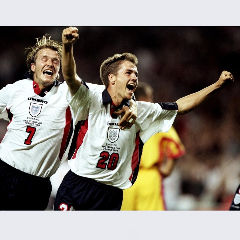 May include: Two soccer players in white jerseys with the text "England FIFA World Cup France 1998" and the numbers "7" and "20" on them, celebrating a goal.