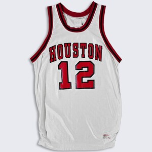 May include: White basketball jersey with red trim and the word "HOUSTON" and the number "12" in red with black outlines.