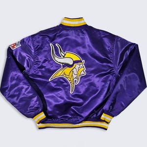 May include: A purple satin jacket featuring the Minnesota Vikings logo on the back. The logo is a yellow and white Viking head. The jacket has yellow and white striped trim on the collar, cuffs, and waist. An NFL patch is on the left sleeve.