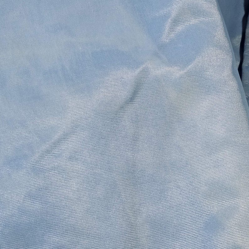 May include: A close-up view of a light blue fabric with a subtle sheen. The material has a fine, textured weave, creating a soft, flowing appearance. The fabric is slightly creased, adding depth and dimension to the overall look. The color is a pale, muted blue.