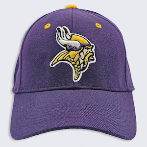 Puede incluir: Gorra de béisbol morada con visera curva y botón amarillo. La gorra presenta un logotipo bordado de una cabeza vikinga en amarillo, blanco y morado.