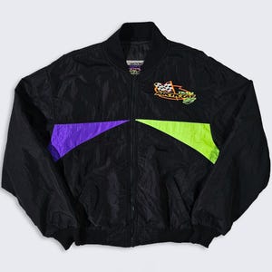 May include: Black nylon jacket with a zip-up front, featuring a purple and neon green colour block design. The jacket has a collar and the text "ARCTIC CAT TEAM" with a checkered flag logo.