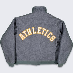 Puede incluir: Una chaqueta de forro polar gris con "ATHLETICS" bordado en amarillo en la parte posterior.