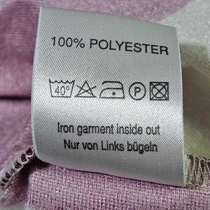 Puede incluir: Una etiqueta de cuidado blanca con texto negro que dice "100% POLYESTER". La etiqueta tambi&eacute;n incluye un conjunto de instrucciones de cuidado: lavar a m&aacute;quina a 40 grados Celsius, no blanquear, planchar a baja temperatura, no limpiar en seco y planchar del rev&eacute;s. El texto "Iron garment inside out Nur von Links b&uuml;geln" tambi&eacute;n est&aacute; incluido.