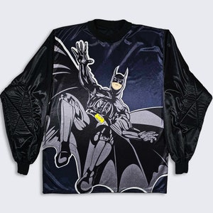 May include: Black long-sleeve shirt with a graphic print of Batman flying. The shirt has a black satin-like fabric with a dark blue background.