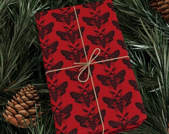 May include: A wrapped gift with a red background and a repeating black moth design. The gift is tied with twine and rests on a bed of green pine needles and pine cones. The moth design has a skull on the moth's head.
