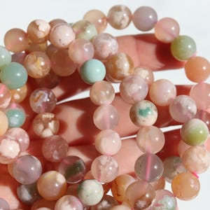 Puede incluir: Una hebra de cuentas de ágata de colores en tonos rosa, verde y naranja. Las cuentas son redondas y tienen un acabado natural y pulido.
