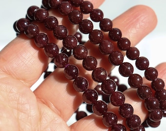 May include: Three strands of dark red gemstone beads, likely garnet, are strung together to form a bracelet. The beads are round and smooth, and they have a slight sparkle to them.