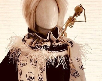 May include: A white mannequin wearing a black and white costume with a skull pattern. The costume has a feathered collar and a skeleton prop on the shoulder.