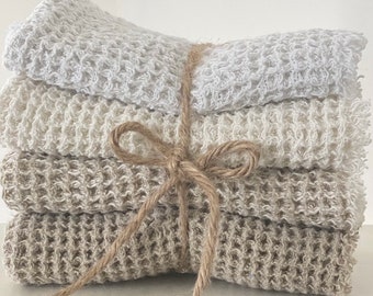 May include: Four folded, textured washcloths in shades of white and beige, bound with twine. The washcloths feature a waffle-weave design. The twine is tied in a bow.