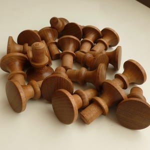 May include: A collection of turned wooden chess pieces, featuring a dark brown finish. The pieces have a classic design with a circular base and a cylindrical body. The pieces are scattered on a light-colored surface.