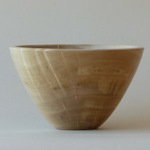 May include: A light brown wooden bowl with a smooth, rounded shape. The bowl is made of wood with a natural grain pattern.