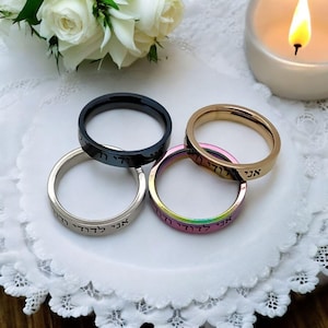 May include: Four thin metal rings with Hebrew writing on them. The rings are stacked on top of each other. The rings are black, silver, gold, and iridescent.
