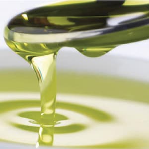 Puede incluir: Una cuchara de vidrio transparente vierte un líquido amarillo dorado en un tazón blanco. El líquido es espeso y viscoso, creando un efecto de ondulación en el tazón.