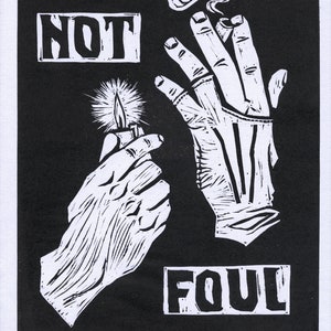 May include: A black and white woodcut print depicting a hand holding a lit cigarette with smoke rising above it. The hand is labelled "NOT" and the other hand is holding a lighter and labelled "FOUL". The title of the artwork is "I'm Not Foul (2019)" and the artist's signature is "Megara".