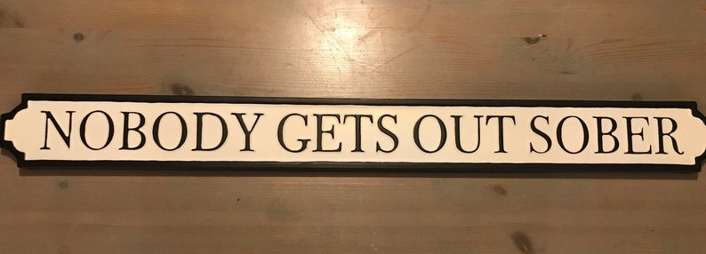May include: Black and white sign with the text "NOBODY GETS OUT SOBER" on a white background.