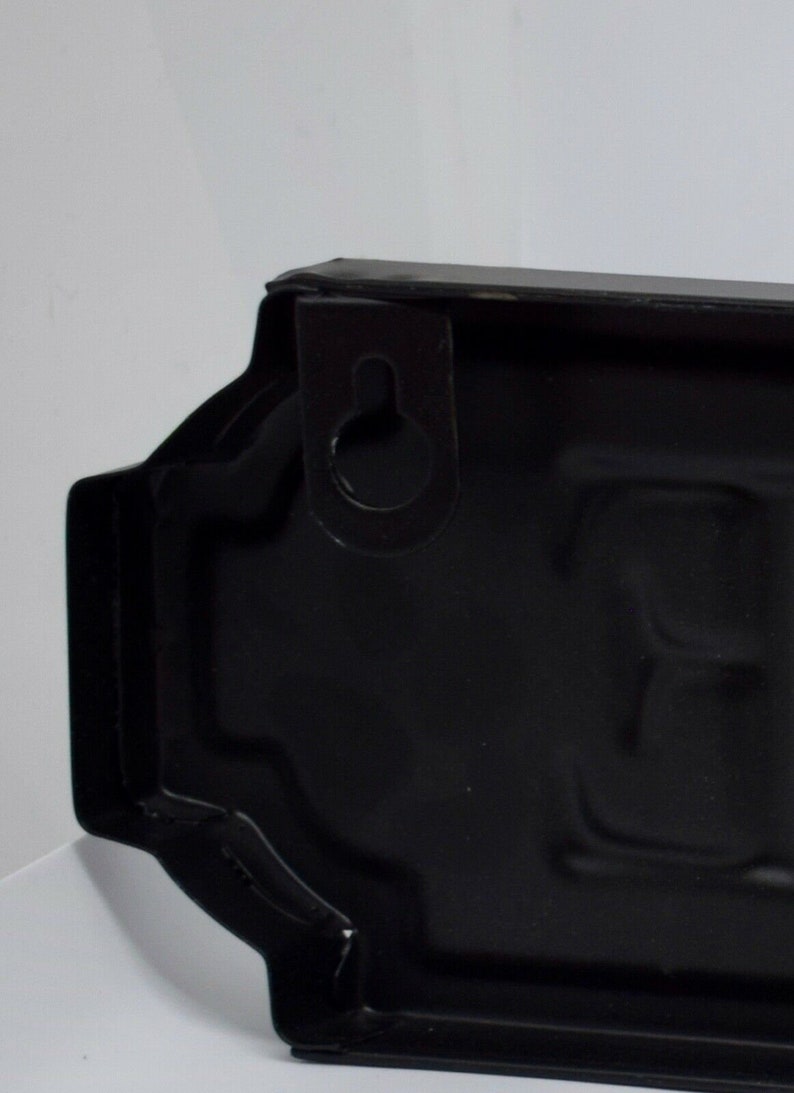 May include: Black metal sign with a rounded rectangular shape and a hanging hole at the top. The sign has a slightly textured surface.