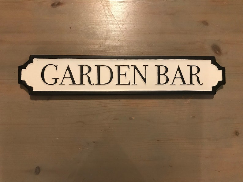 May include: Black and white sign with the text "GARDEN BAR" in black lettering on a white background. The sign has a black border and rounded edges.