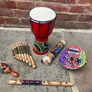 Può includere: Un set di strumenti musicali colorati che includono un tamburo rosso, uno xilofono in legno, una maraca, un flauto di bambù e un kalimba. Gli strumenti sono decorati con motivi intricati.