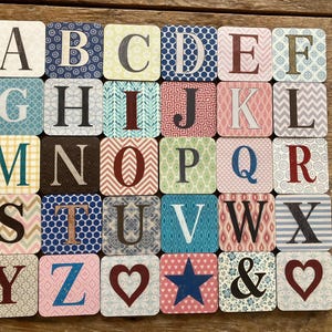 May include: A set of 28 square alphabet tiles, each with a different letter, number, or symbol. The tiles have patterned backgrounds in colours like blue, pink, and green. The letters are in a serif font.