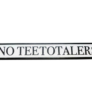 May include: A white sign with black lettering that reads "NO TEETOTALERS". The sign is shaped like a street sign with rounded edges.