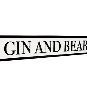 May include: A white sign with black lettering that reads "GIN AND BEAR IT". The sign is shaped like a traditional street sign with rounded edges.