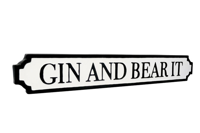 May include: A white sign with black lettering that reads "GIN AND BEAR IT". The sign is shaped like a traditional street sign with rounded edges.
