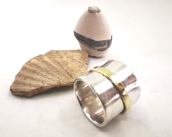 May include: A silver and gold spinning ring with a hammered finish. The ring is made of two bands, one silver and one gold, that spin independently.