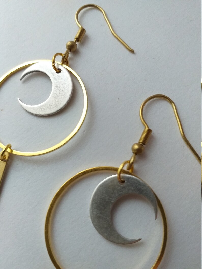 Op de afbeelding: Goudkleurige metalen oorbellen met een halve maan ontwerp. Elke oorbel heeft een goudkleurige cirkel met een zilverkleurige halve maan bedel. De oorbellen hebben een eenvoudige haaksluiting.