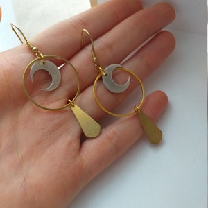 Op de afbeelding: Een paar goudkleurige oorbellen met een maanmotief. Elke oorbel heeft een gouden ring, een zilveren halve maan en een druppelvormige hanger. De oorbellen worden gepresenteerd tegen een lichte achtergrond.