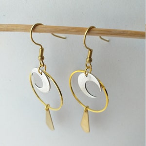 Op de afbeelding: Een paar goudkleurige oorbellen met een hemels thema. Elke oorbel heeft een gouden ring, een zilveren halve maan en een kleine gouden driehoekige hanger. De oorbellen zijn opgehangen aan goudkleurige oorhaken.