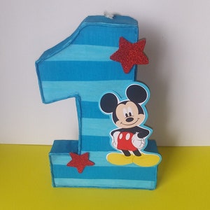 Puede incluir: Una pi&ntilde;ata de cart&oacute;n n&uacute;mero uno con rayas azules y blancas, una estrella roja y un personaje de Mickey Mouse.