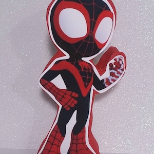 May include: A red and black cartoon figure of Spider-Man with a white face and red eyes. The figure is standing with its right arm raised and its left hand on its hip.