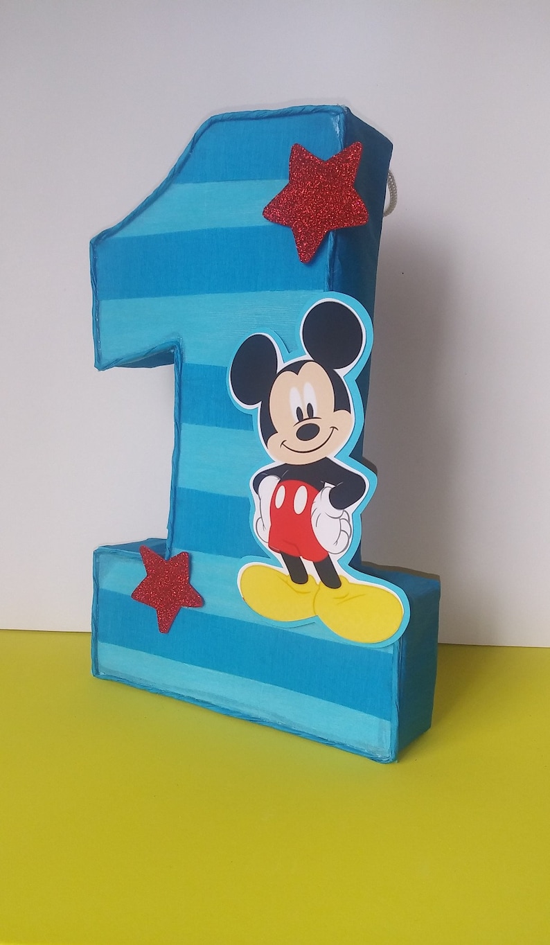 Puede incluir: Pi&ntilde;ata de cart&oacute;n n&uacute;mero uno con rayas azules y blancas, una estrella roja y un personaje de Mickey Mouse en la parte delantera.