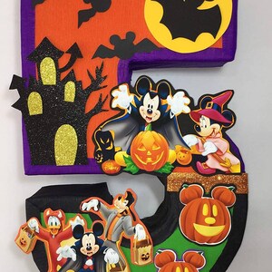 May include: A Halloween-themed number five piñata featuring Mickey Mouse and friends dressed in costumes. The piñata is decorated with bats, a haunted house, and pumpkins. The text "Disney" is visible on the piñata.