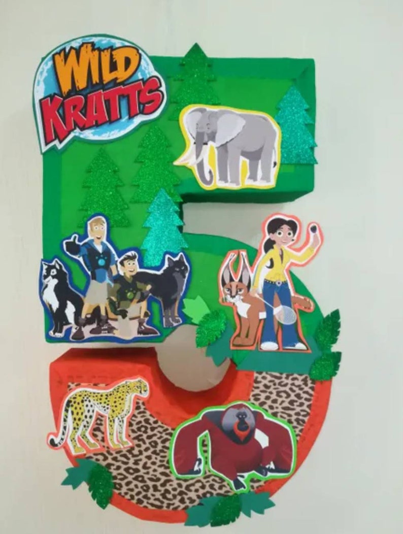 Peut inclure: Un chiffre cinq en carton vert d&eacute;cor&eacute; de personnages et d'animaux Wild Kratts. Le chiffre est d&eacute;cor&eacute; d'arbres verts, d'un gu&eacute;pard, d'un &eacute;l&eacute;phant, d'un gorille et d'un chat. Le chiffre est d&eacute;cor&eacute; d'un motif l&eacute;opard.