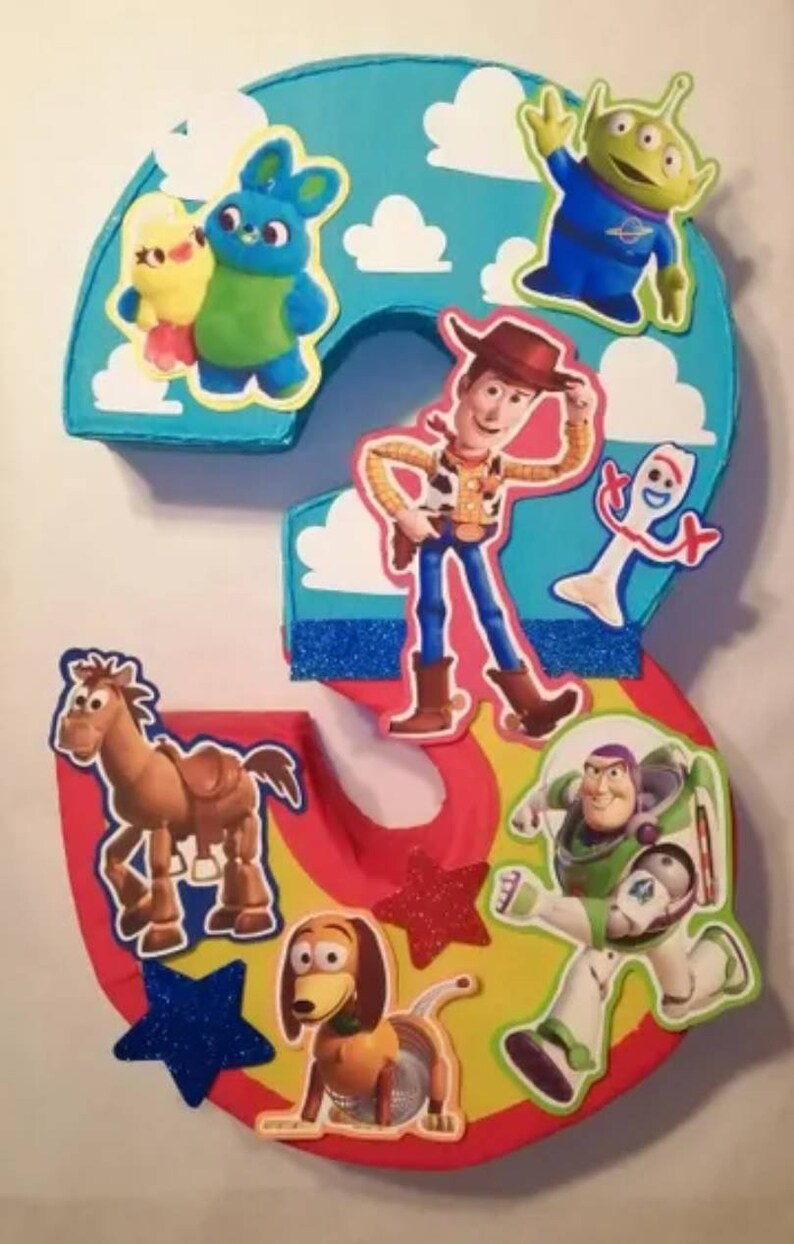 May include: A colorful number three decoration featuring characters from the Toy Story movie. The number is primarily blue, red, and yellow, with character cutouts including Woody, Buzz Lightyear, and the Little Green Men.
