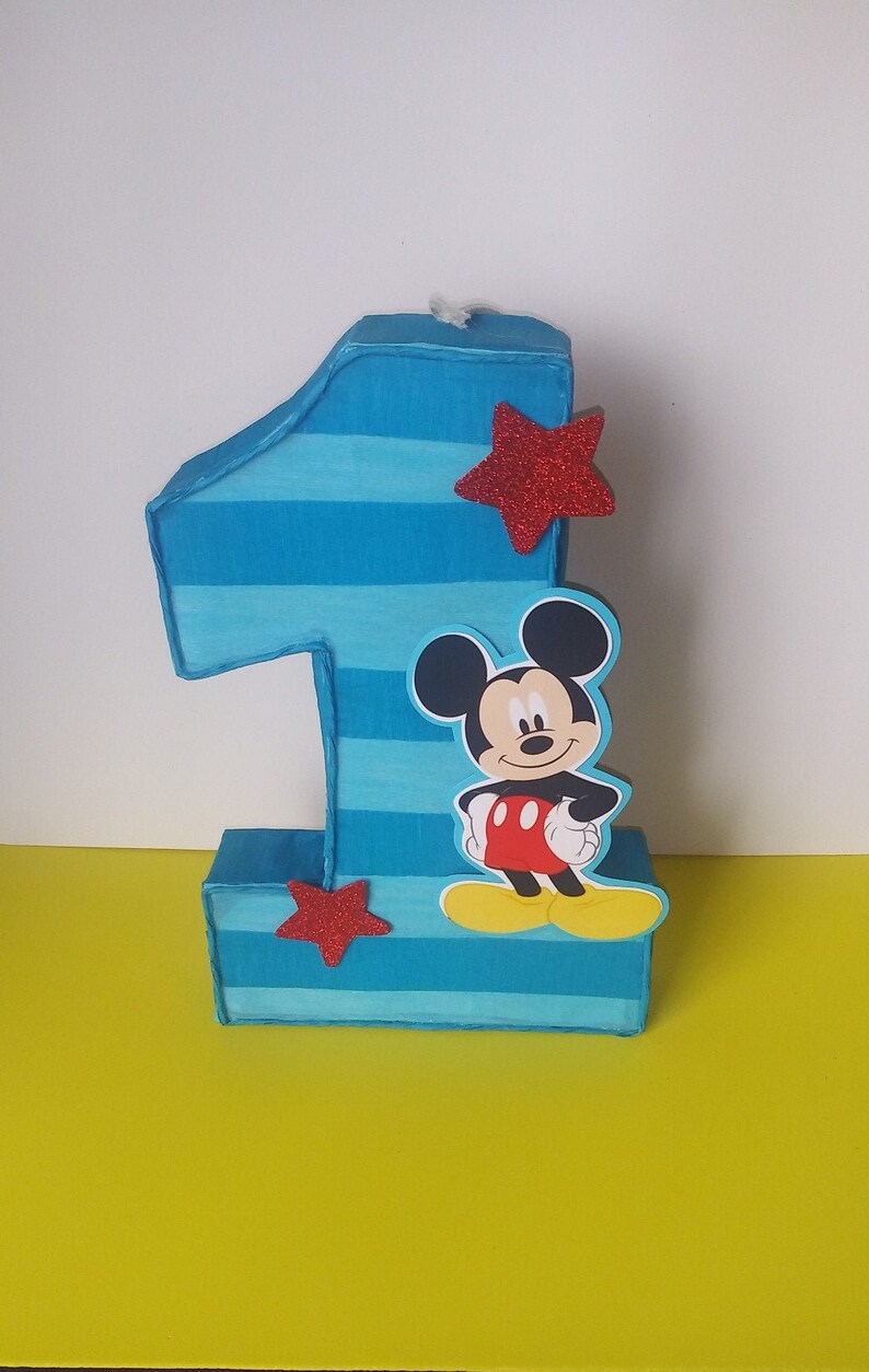Puede incluir: Una pi&ntilde;ata de cart&oacute;n n&uacute;mero uno con rayas azules y blancas, una estrella roja y un personaje de Mickey Mouse.