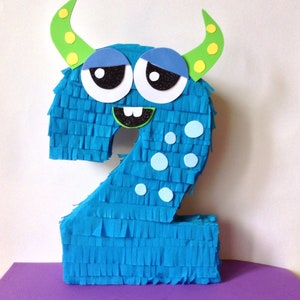 May include: A blue monster shaped like the number two. The monster has green horns with yellow dots, blue eyes, a black mouth with white teeth, and white polka dots.