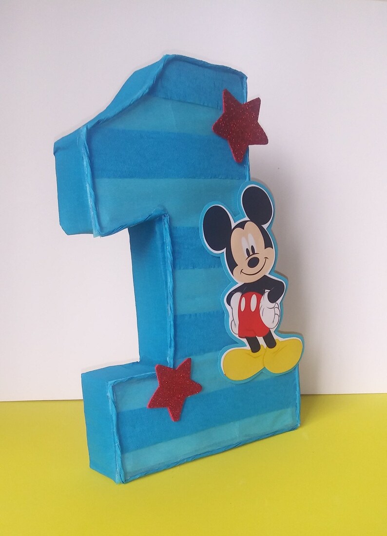 Puede incluir: Un n&uacute;mero uno de cart&oacute;n a rayas azules y blancas con una estrella roja y un personaje de Mickey Mouse.
