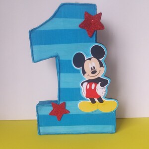 Puede incluir: N&uacute;mero uno de cart&oacute;n a rayas azules y blancas con una estrella roja y un recorte de personaje de Mickey Mouse.
