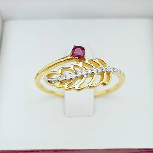 Può includere: Un anello d'oro con una pietra preziosa di rubino e un design a foglia con piccoli diamanti.