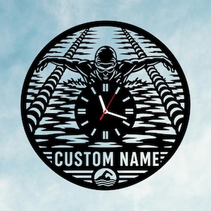 Könnte beinhalten: Eine kreisförmige schwarze Wanduhr mit einem lasergeschnittenen Design eines Schwimmers in einem Becken mit Bahnen. Die Mitte zeigt ein Zifferblatt mit weißen Markierungen und Zeigern, während der Text CUSTOM NAME unten mit einem Symbol steht.